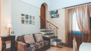 A living room with a sofa, a lamp, a staircase, and artwork on the walls. - Lubra Casa Relax (Massa lubrense)