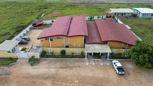 A large building with a red roof, a parking area, and a small red structure nearby. - Florence Hotel Firenze Yamoussoukro (Yamoussoukro)