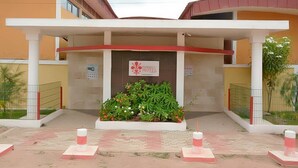 A hotel entrance with a red and white sign, a covered waiting area, and a landscaped garden. - Florence Hotel Firenze Yamoussoukro (Yamoussoukro)