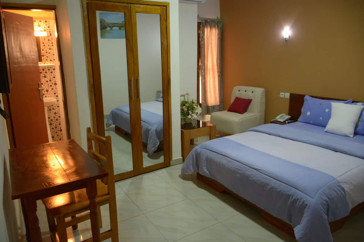 A hotel room with a bed, a chair, a table, and a mirror.