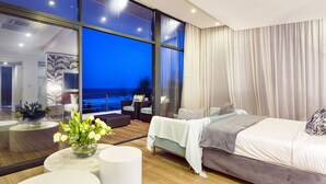 Une chambre d’hôtel moderne dotée d’une grande fenêtre donnant sur l’océan, avec une vue particulièrement belle la nuit.