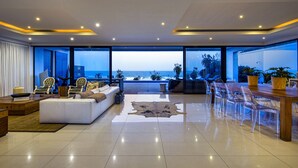 Un vaste espace de vie avec une grande fenêtre donnant sur l’océan, un canapé moderne, une table à manger avec des chaises et une vue sur la plage.