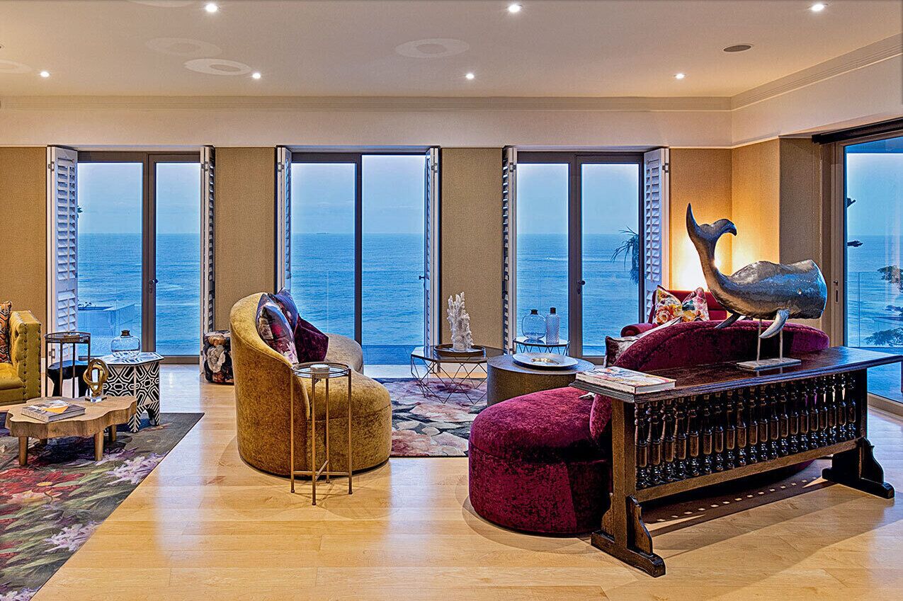 A spacious living room with a large window offering a view of the ocean. There is a plush red sofa, a yellow armchair, and a wooden coffee table.