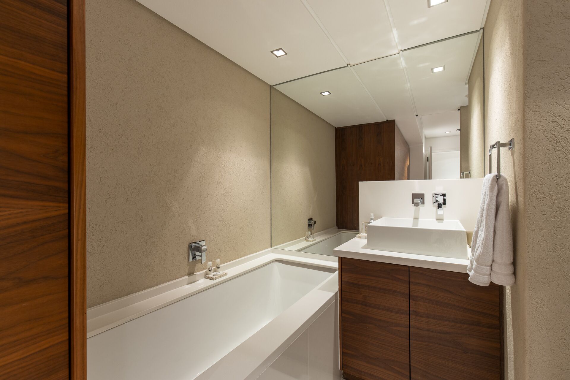 Un baño moderno con una bañera grande, un tocador de madera y un espejo sobre el lavabo.