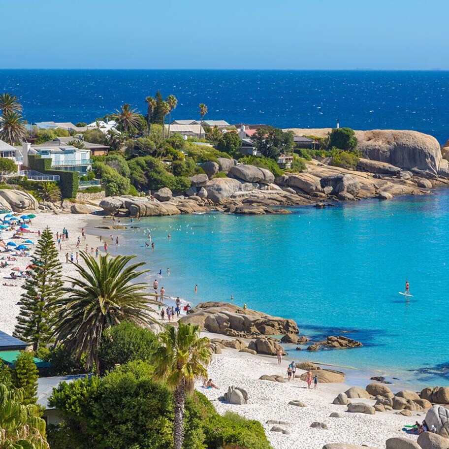 A coastal beach with clear blue waters, rocky shorelines, and a variety of beach umbrellas.