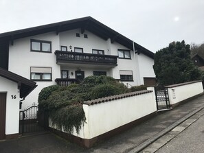 Un edificio blanco de dos pisos con balcón, portón y el número 16 en la fachada.