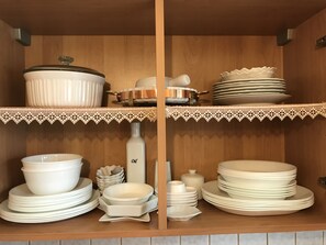 Una cocina con estantes de madera que exhiben diversos platos de cerámica blanca, incluyendo tazones, platos y una olla.
