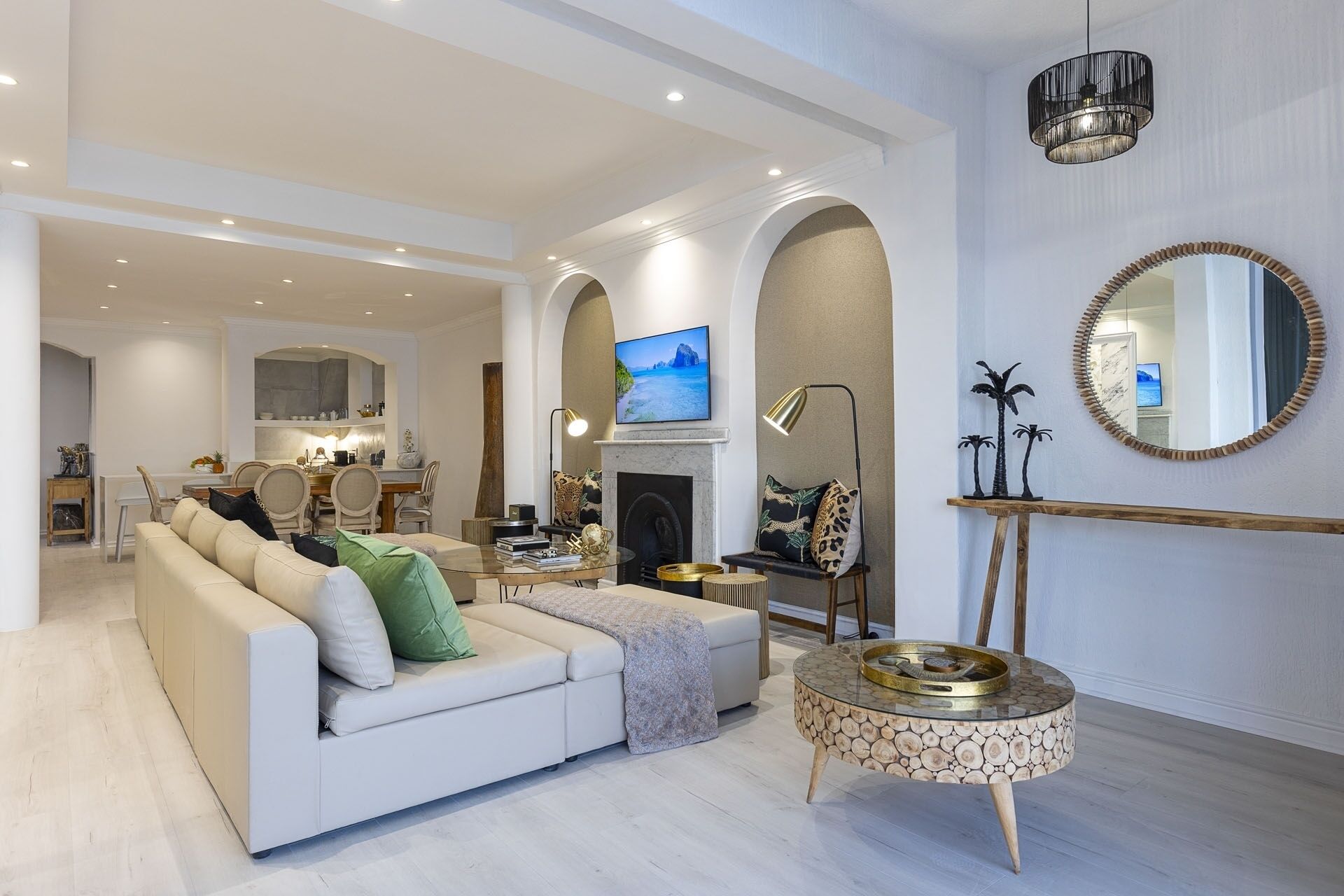 A spacious living room with a white sofa, a fireplace, and a television mounted on the wall.