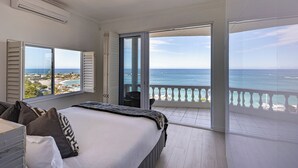 Ein Schlafzimmer mit einem großen Bett, Meerblick und einem Balkon mit Geländer.