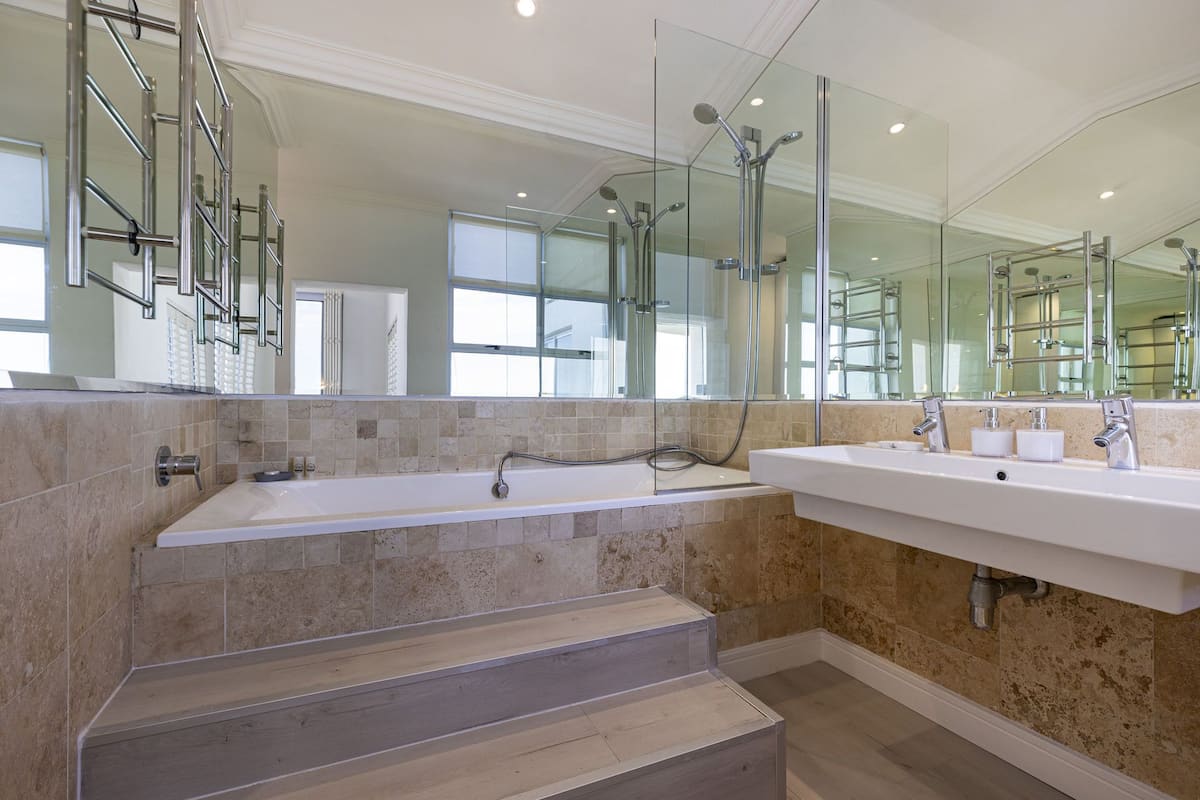 A modern bathroom with a large bathtub, two sinks, and a glass shower enclosure.