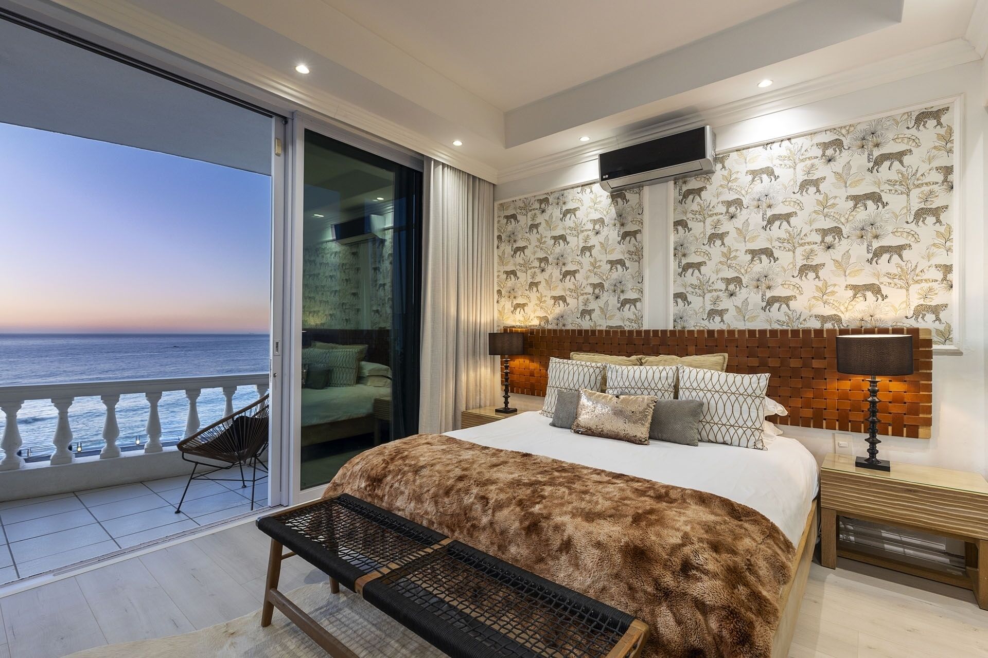 A bedroom with a large bed, a view of the sea, a balcony with a chair, and a patterned wallpaper.