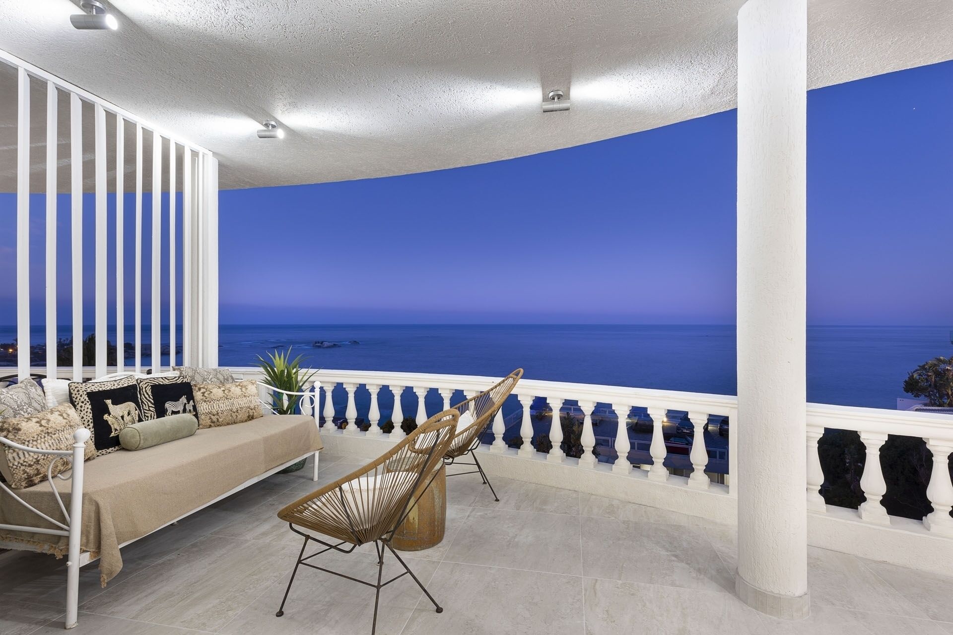 A balcony with a curved ceiling, a sofa with patterned cushions, and a wicker chair.