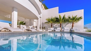 Ein moderner Poolbereich mit klarem, blauem Wasser, weißen Liegestühlen und Palmen.