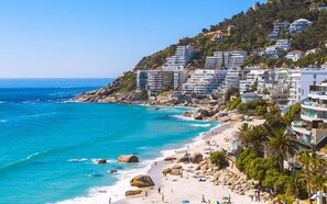 A coastal cityscape with a beach, rocky shoreline, and buildings with balconies overlooking the sea.