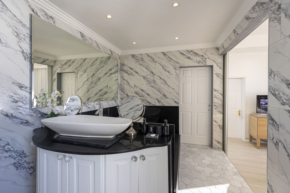 A bathroom with a white sink, marble walls, and a large mirror.