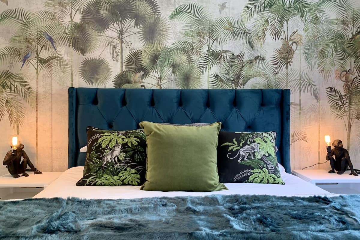 A bedroom with a tufted headboard, a plush fur rug, and a mural of tropical foliage.