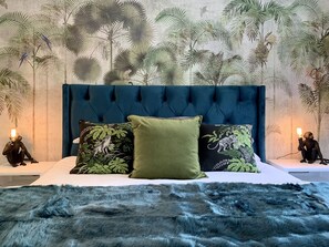 A bedroom with a tufted headboard, a plush fur rug, and a mural of tropical foliage. - Clifton YOLO Spaces – Clifton Boutique Apartments  (Cape Town)