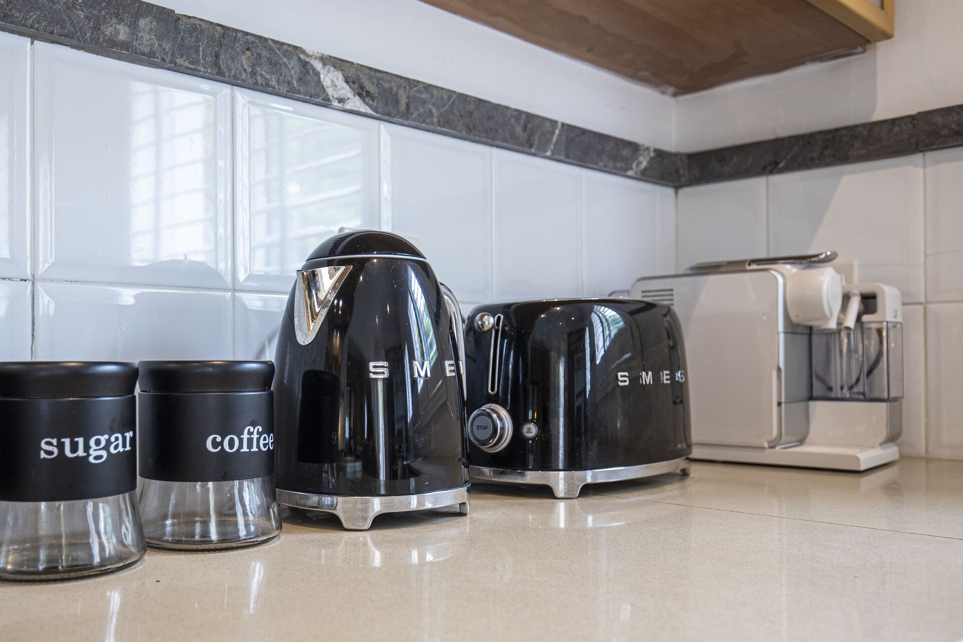 A kitchen with a coffee maker, sugar and coffee containers, a toaster, and a kettle.