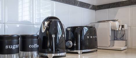 A kitchen with a coffee maker, sugar and coffee containers, a toaster, and a kettle.