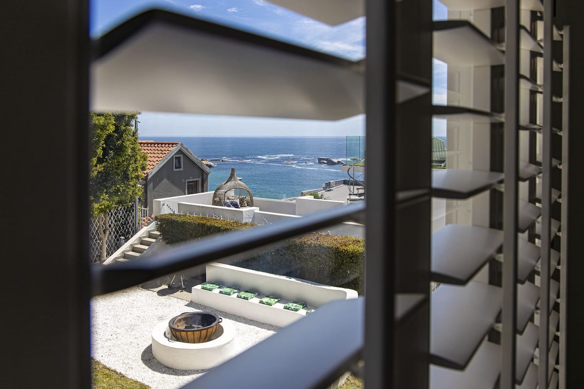 A balcony with a view of the ocean, a small garden area with a fire pit, and a building with a unique architectural design.