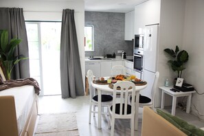 A modern kitchen with white cabinets, a dining table with chairs, and a small side table with a plant.