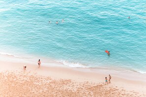 A beach with people swimming and standing on the sand.