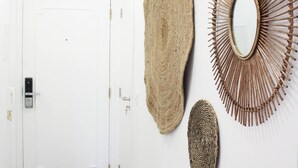 Un couloir avec une porte blanche, une décoration murale texturée et un miroir en forme de soleil.