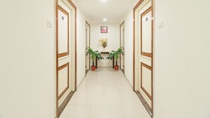 A hallway with two potted plants, a framed picture on the wall, and a light fixture on the ceiling. - Octave Church Inn (Bengaluru)