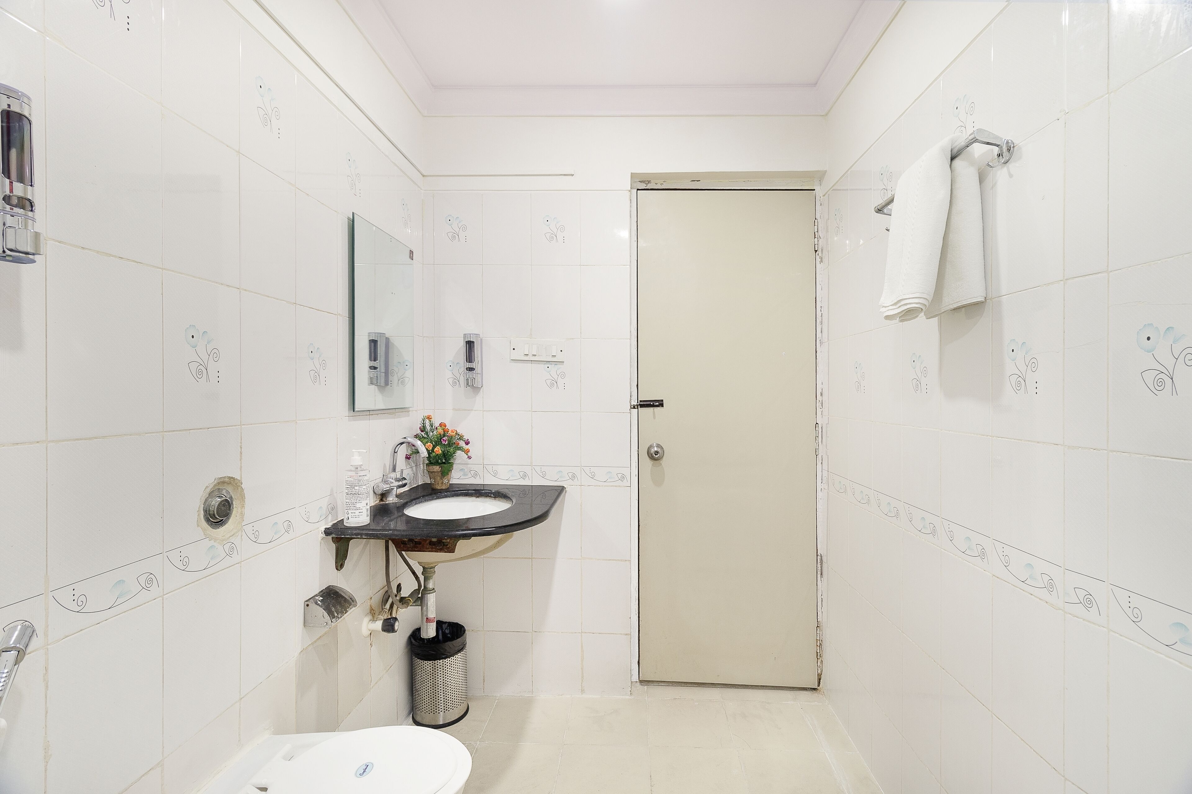 A bathroom with a white sink, toilet, and a door with a towel hanging on the wall.