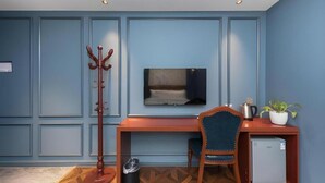 A room with a wooden desk, a chair, a television, a coat rack, a small refrigerator, and a potted plant. - Yiting Zhenshe Hotel (Beijing)