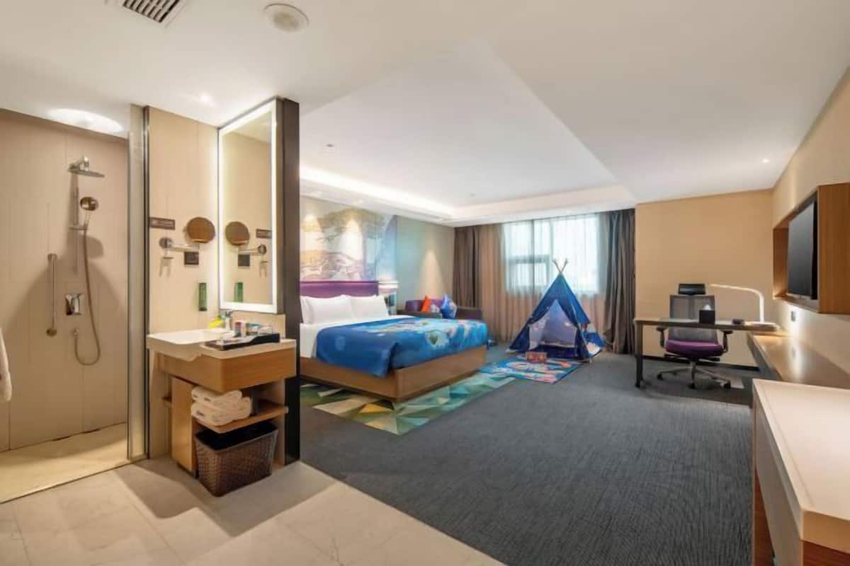 A hotel room with a bed, a desk, a chair, a shower, and a large mirror.