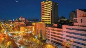 A cityscape at night with illuminated buildings, a crescent moon, and a busy road with vehicles. - Hampton by Hilton Fuyang Guomao (Fuyang)