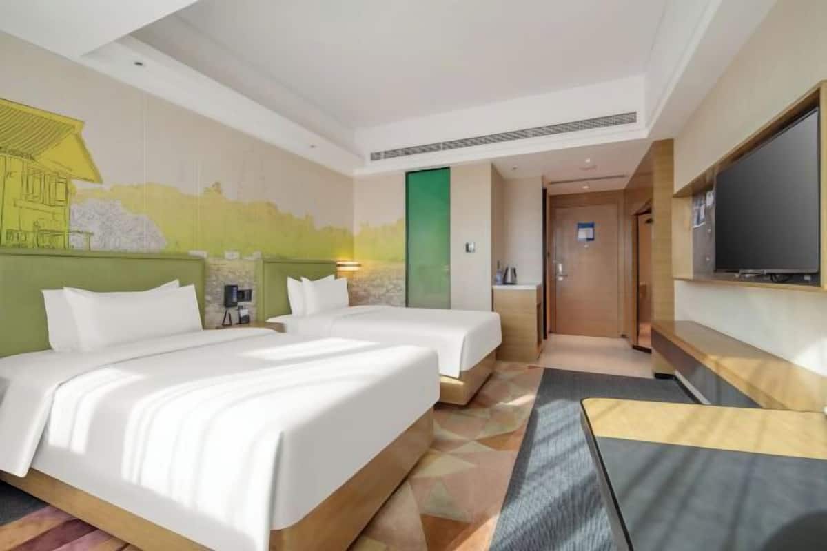A hotel room with two beds, a television, a desk, and a mural on the wall.