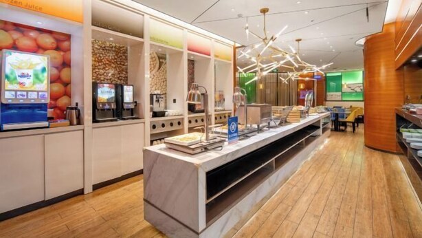 A modern cafe with a long counter, coffee machines, and a digital menu display. - Hampton by Hilton Fuyang Guomao (Fuyang)