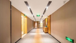 A hotel corridor with wooden walls, a carpeted floor, and a reception desk with a green exit sign. - Hampton by Hilton Fuyang Guomao (Fuyang)