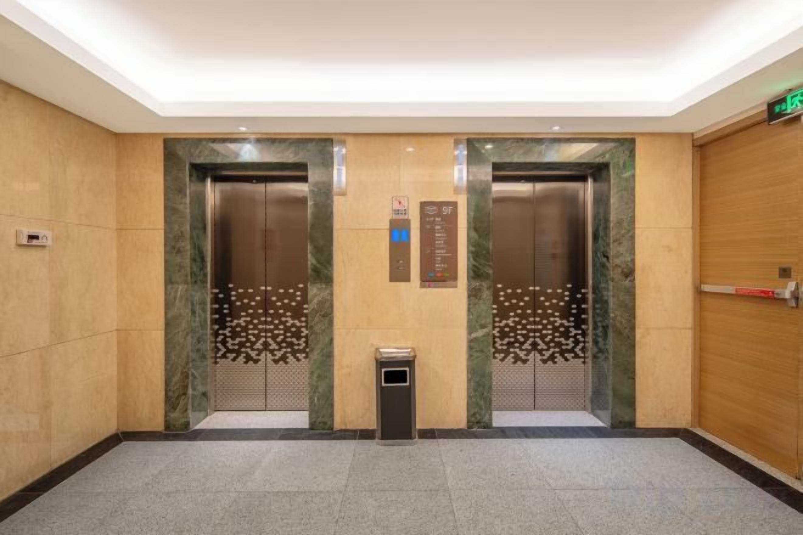 An elevator area with two elevators, a trash bin, and a wooden wall.