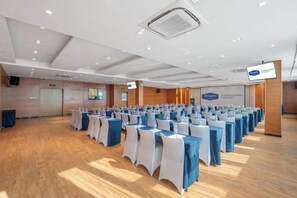 Een congrescentrum met rijen tafels en stoelen, een podium met een scherm en een houten vloer.