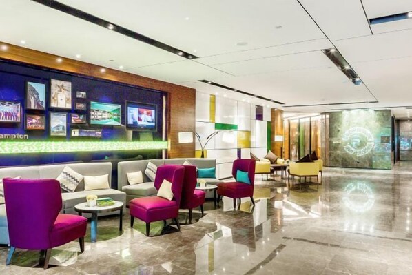 Un moderno vestíbulo con diversas opciones de asientos, incluyendo sofás y sillones, y una pared decorada con cuadros enmarcados y una pantalla digital.