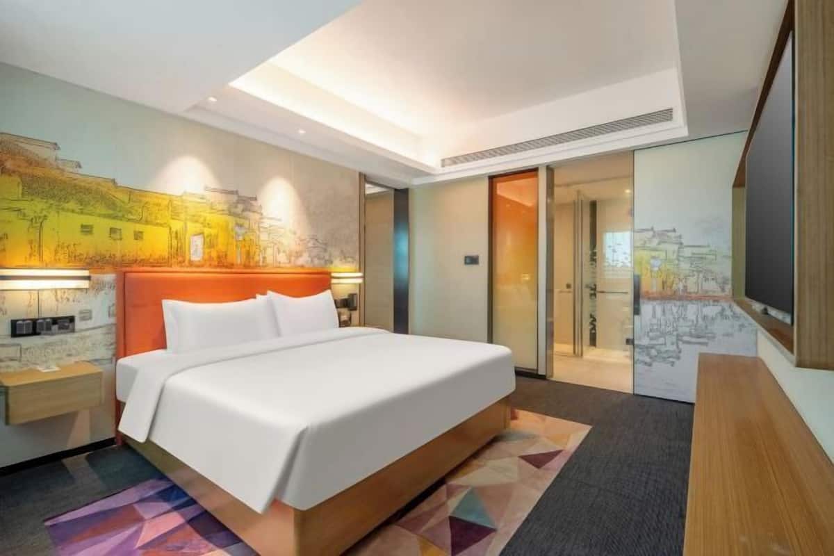 A hotel room with a bed, a nightstand, a desk, a chair, a TV, and a door.