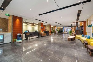 A hotel lobby with a reception desk, seating area, and a self-service kiosk.