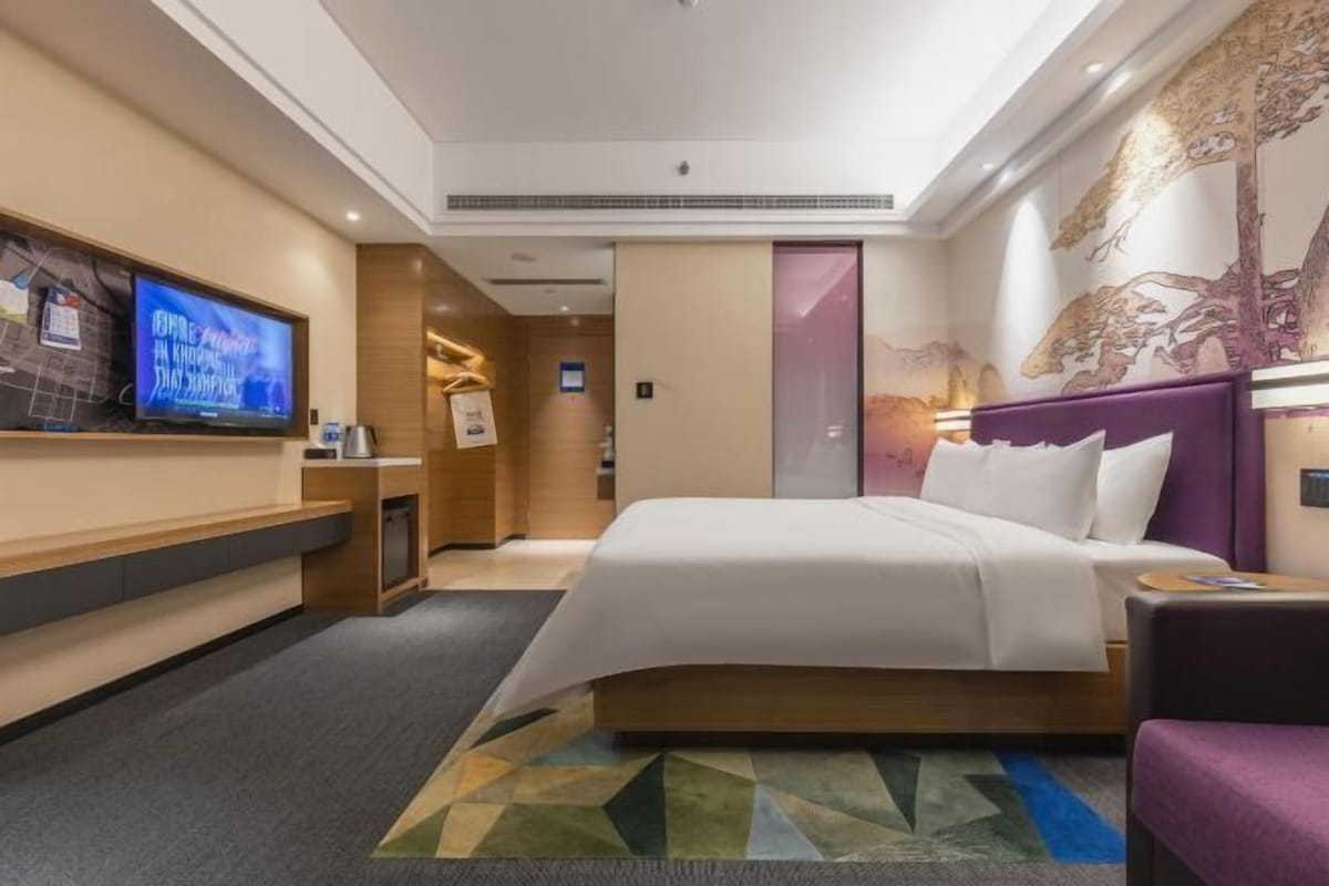 Una habitación de hotel moderna con una cama grande, un televisor en la pared y un mural decorativo.