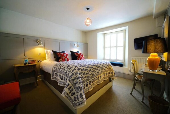 A bedroom with a bed, bedside tables, a chair, a desk, a lamp, and a window.