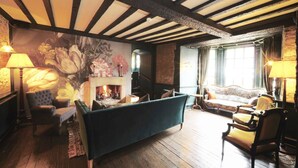 A cozy living room with a fireplace, wooden beams, a sofa, and a chair. - The Bull Hotel (Fairford)