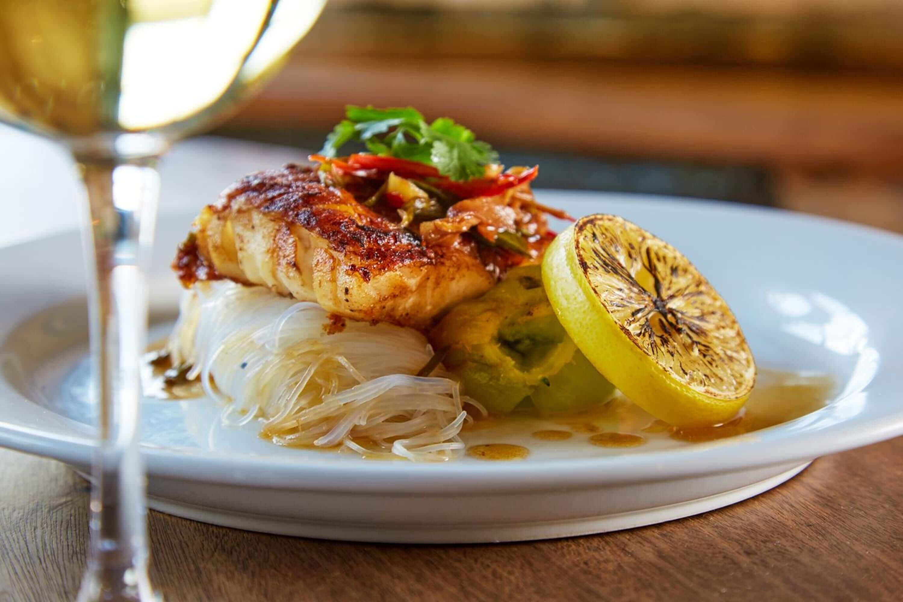 A plate of food with grilled chicken, vegetables, and a lemon slice.