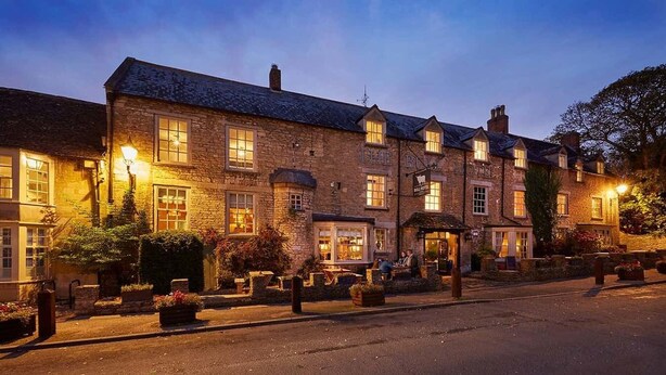 A traditional stone building with multiple windows and a pub sign, suggesting a pub or restaurant. - The Bull Hotel (Fairford)