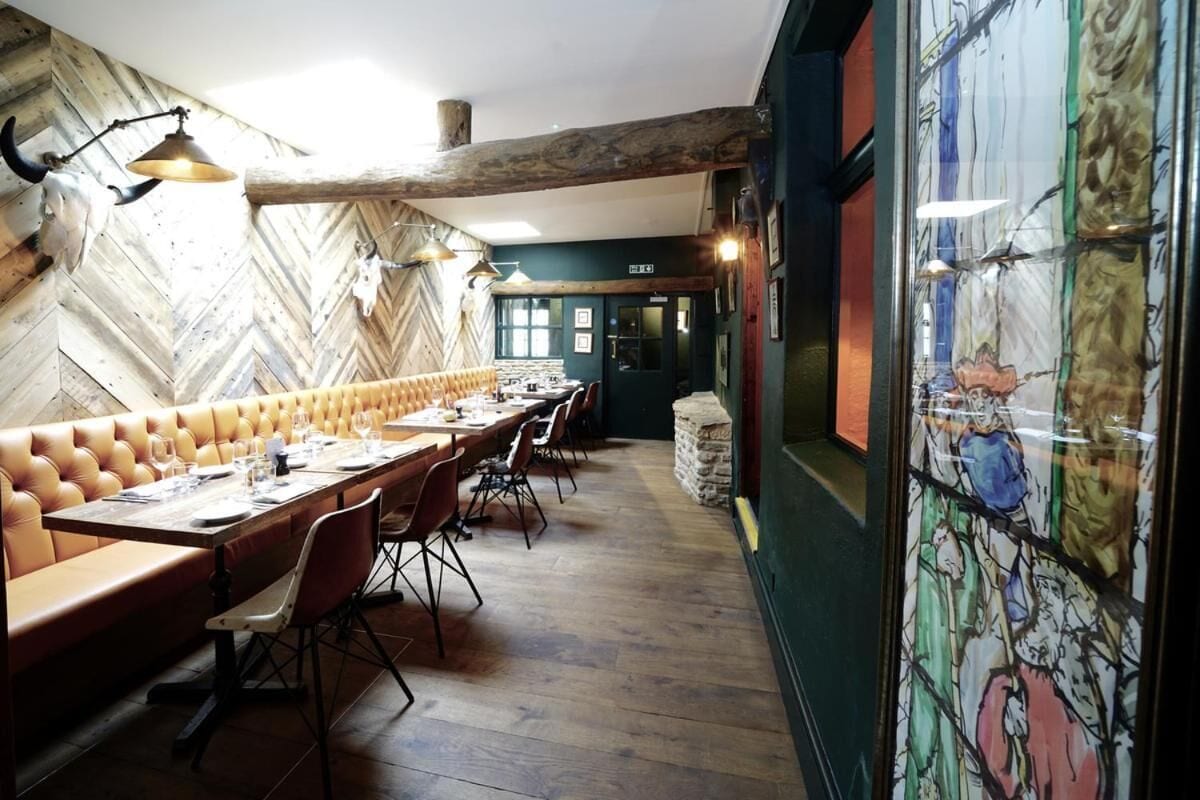 A restaurant with wooden walls, a long bench seating area, and a mural on the right wall.