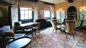 A cozy room with a stone wall, a sofa, a dining table, chairs, and a patterned rug. - The Bull Hotel (Fairford)