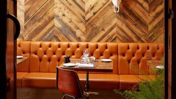 Un interior acogedor con una pared de madera en espiga, un sofá de cuero, una mesa de comedor con sillas y un cuerno decorativo en la pared.