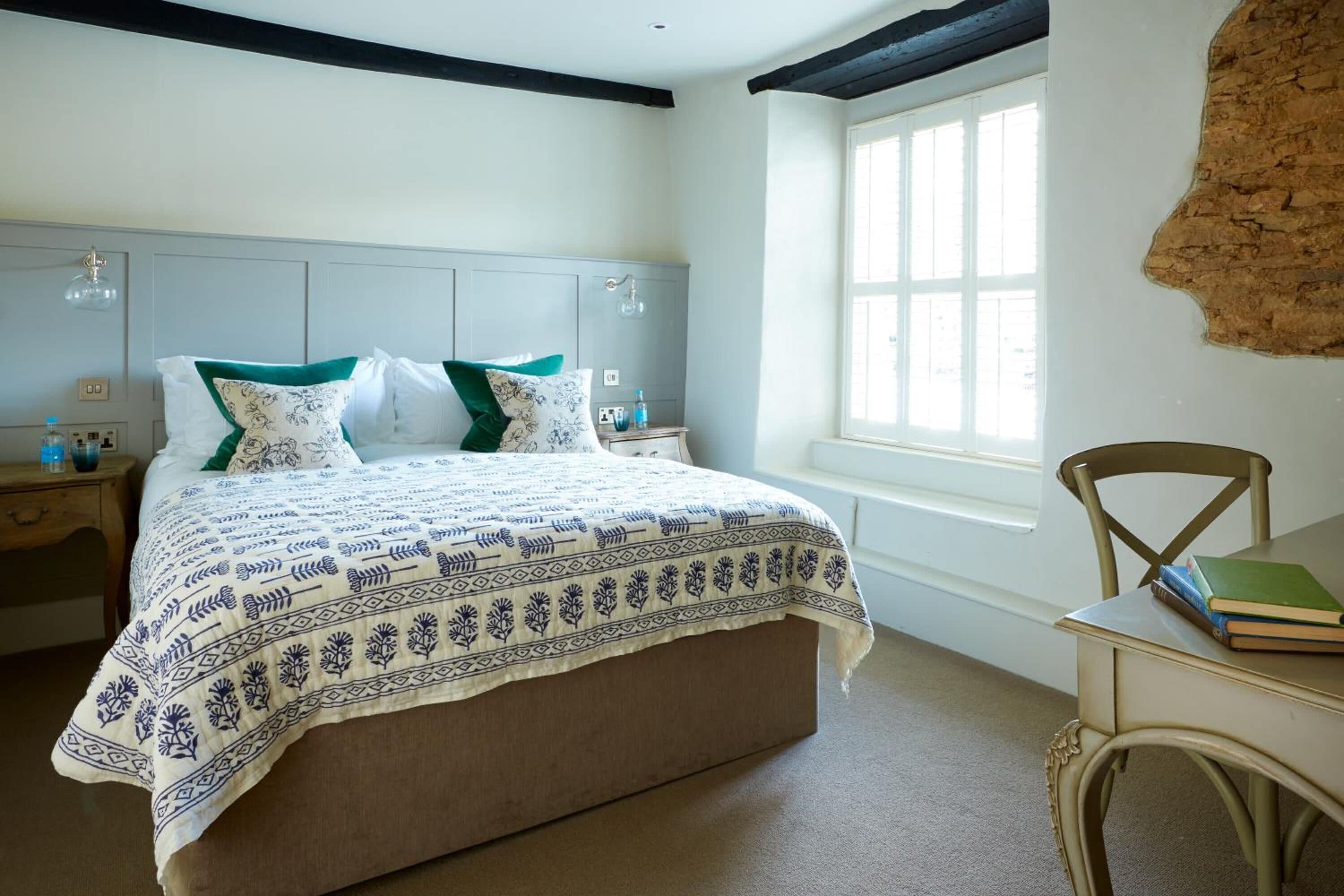 A bedroom with a large bed, a wooden nightstand, a chair, and a window with a view.