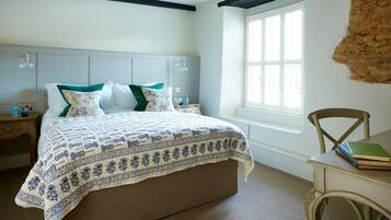 A bedroom with a large bed, a wooden nightstand, a chair, and a window with a view.